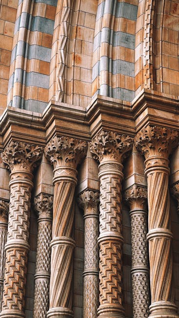 Close-up view of the ornate stone architecture of a historic building, featuring intricately carved columns with spiral and geometric patterns, set beneath a series of vertical stone panels with multicoloured, textured finishes in shades of beige, gray, and light green. The columns are positioned in front of a decorative stone balustrade, and the detailed carvings highlight craftsmanship typical of Gothic or Romanesque styles. The overall scene captures the craftsmanship and texture of the stone, with a focus on the craftsmanship and intricate details of the architectural features, illustrating the historic and artistic element of the structure which could be part of a cathedral or similar heritage building. The environment appears to be outdoor, with natural daylight illuminating the textured surfaces of the stone. This detailed observation aligns with the context of alternative waste handling or on-site clearance related to historical or architectural structures, and might be visible during building restoration or preservation activities such as those offered by independent waste removal services like Rubbish Clearance South Kensington.